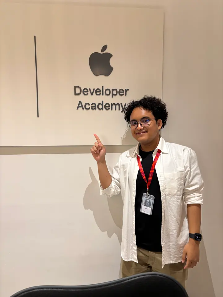 Adrian pointing at the Apple Developer Academy sign, wearing a lanyard