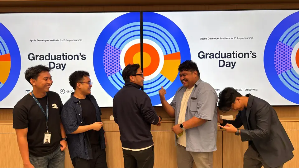 Adrian, his teammates and their mentor laughing in front of the Graduation’s Day screen