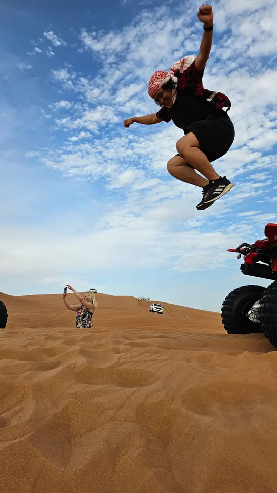 Adrian mid-jump above a sand dune on a desert safari, quad bike behind