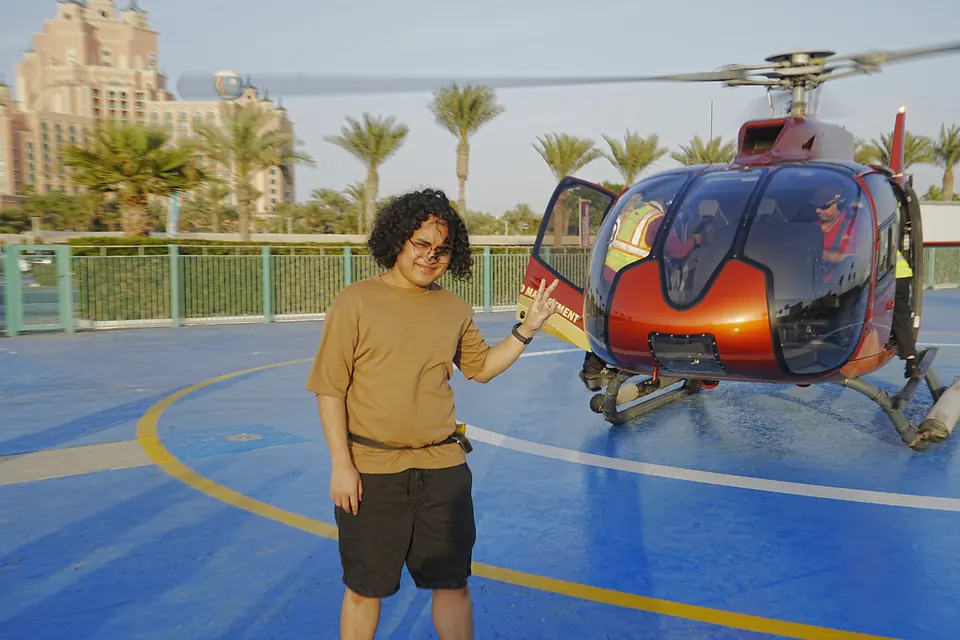 Adrian standing on a blue helipad beside a red helicopter, Atlantis The Palm behind