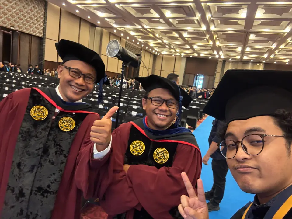 Selfie of Adrian in his cap, with two deans in maroon gowns giving thumbs up