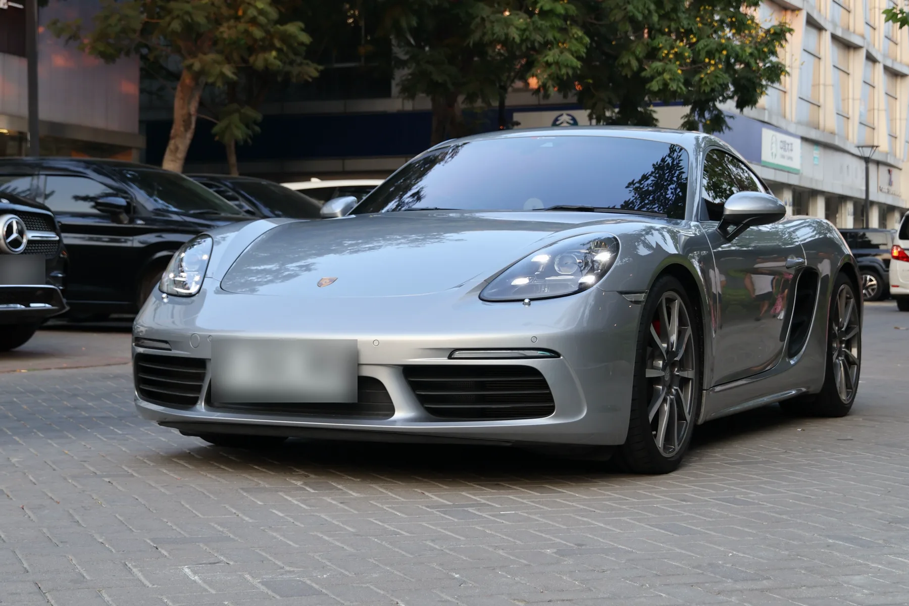 Before: a silver Porsche Cayman on a brick forecourt in flat afternoon light, trees and an office block behind
